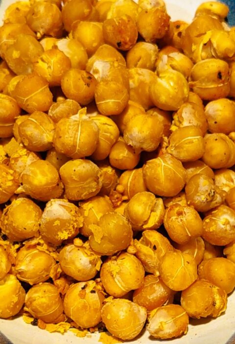 Crispy roasted chickpeas seasoned with herbs in a handmade pottery bowl with dark blue glaze and white details.