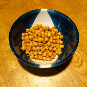 Here are the image details for your roasted chickpeas photo: Alt Text: Crispy roasted chickpeas seasoned with herbs in a handmade pottery bowl with dark blue glaze and white details.