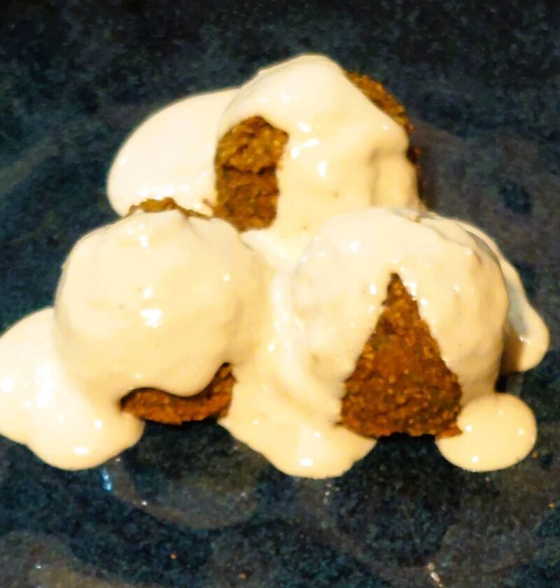 Three falafels covered in creamy tahini sauce served on a handmade dark blue glazed plate.