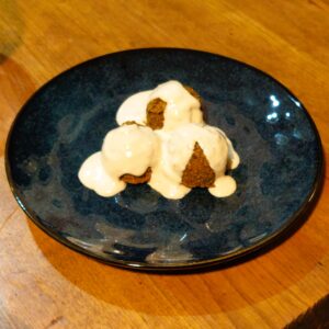 Three falafels covered in creamy tahini sauce served on a handmade dark blue glazed plate.