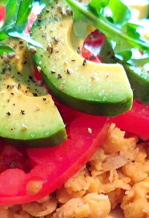 Close-up of a protein-packed plant-based meal featuring mashed chickpeas topped with sliced avocado, fresh tomato, and arugula, seasoned with salt and black pepper.